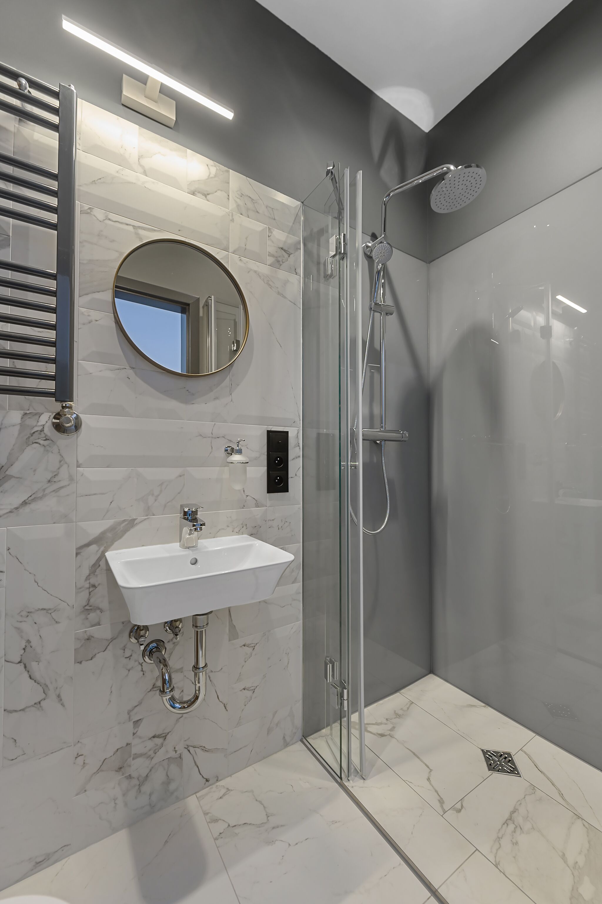 Une salle de bain moderne avec une douche à parois de verre, un lavabo blanc et un sol carrelé en marbre.