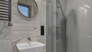 Une salle de bain moderne avec une douche à parois de verre, un lavabo blanc et un sol carrelé en marbre.
