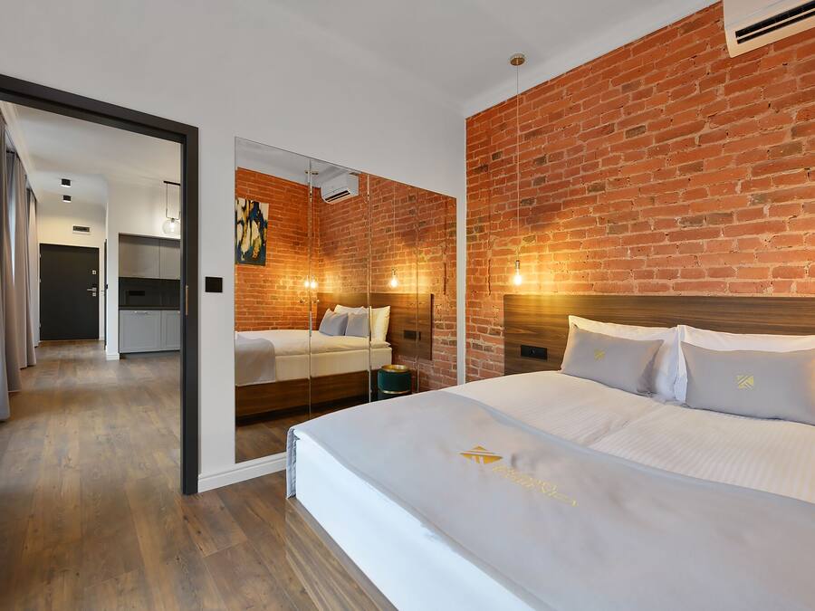 Una habitación de hotel moderna con pared de ladrillo, una cama grande con ropa de cama blanca y una pared de vidrio que separa el dormitorio de la sala de estar.