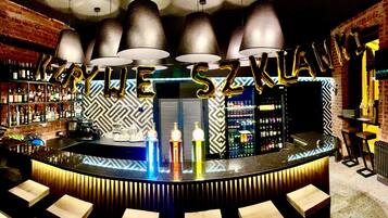 A bar with a modern design, featuring a black and white patterned wall, a central bar counter, and a selection of bottles and glasses.