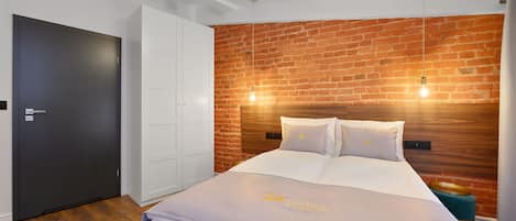A modern bedroom with a brick wall, a large bed with white bedding, a wardrobe, and a door.