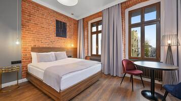 A hotel room with a brick wall, a large bed, a round table, and a chair.
