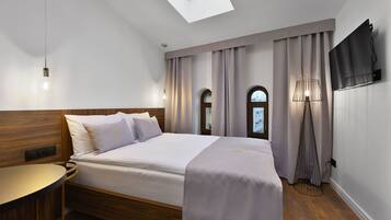 Quarto de hotel moderno com claraboia, uma cama com cabeceira, mesa de cabeceira, abajur e televisão na parede.