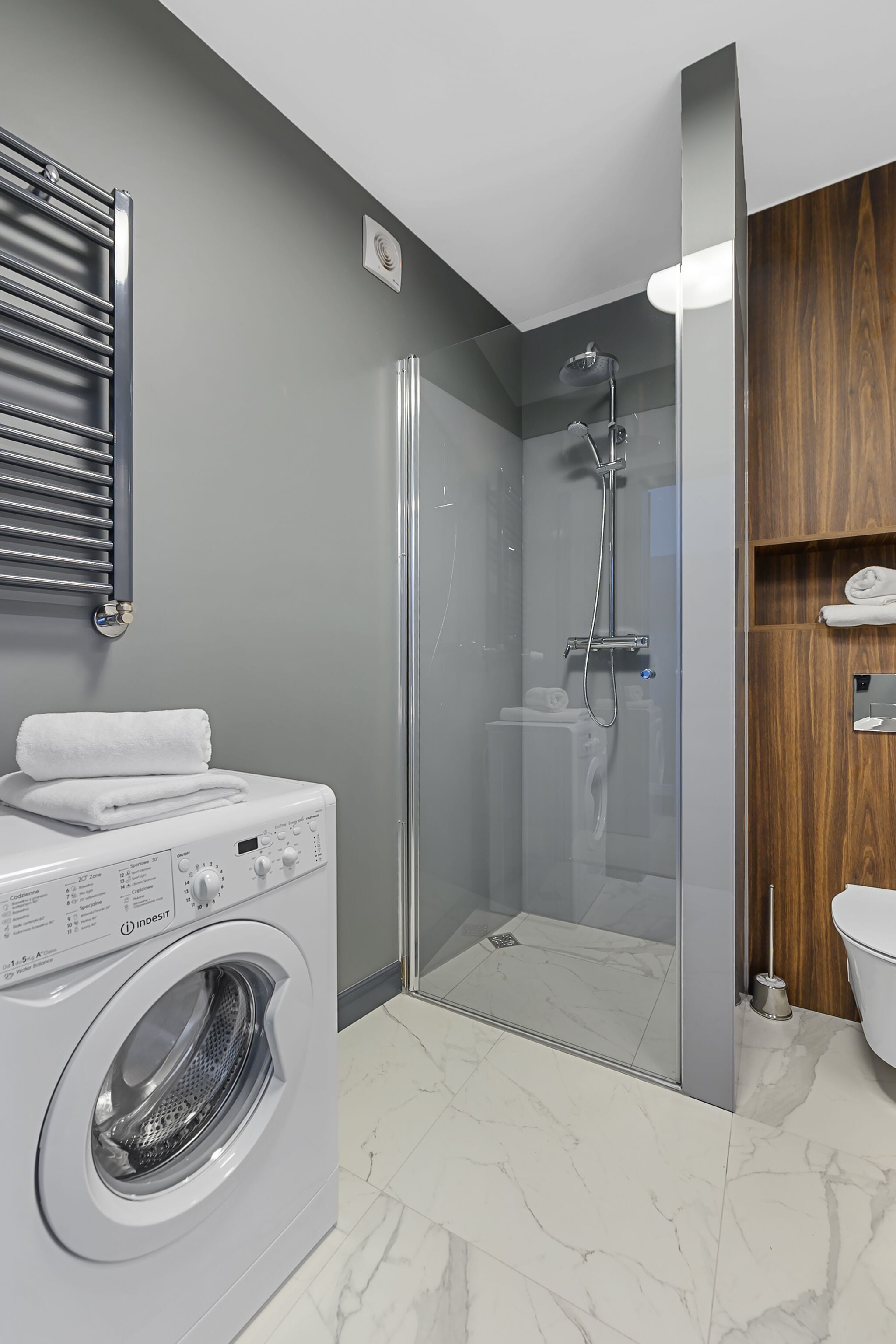 Ein modernes Badezimmer mit Duschkabine, integriertem Waschmaschine und Holzwaschtisch.