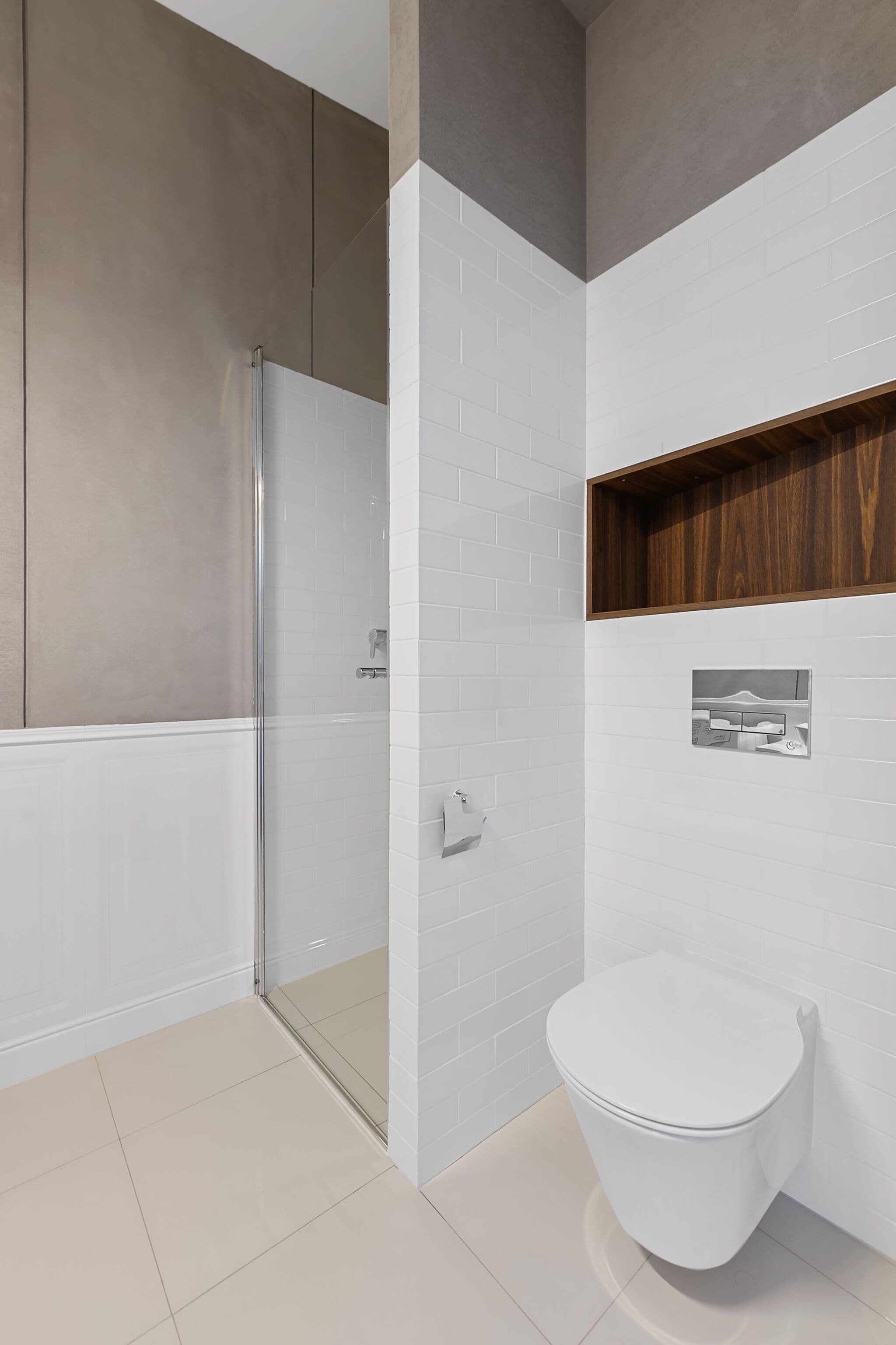 A modern bathroom with a glass shower enclosure, a white toilet, and a wooden shelf.