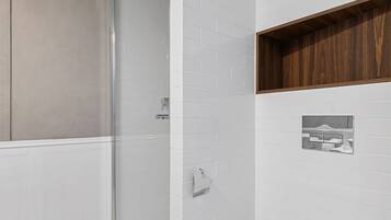 A modern bathroom with a glass shower enclosure, a white toilet, and a wooden shelf.