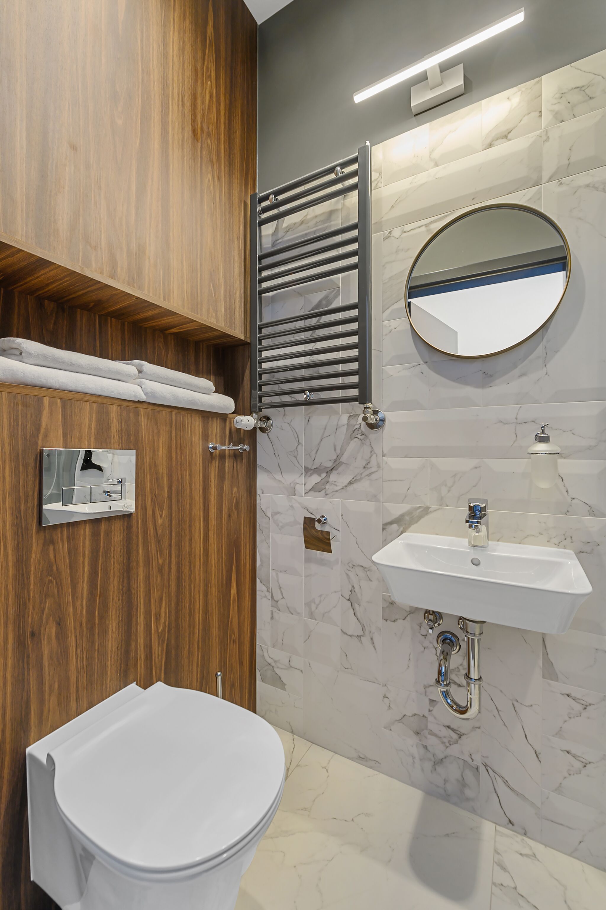 Un baño moderno con tocador de madera, inodoro, lavamanos con salpicadero de mármol y barra para toallas.