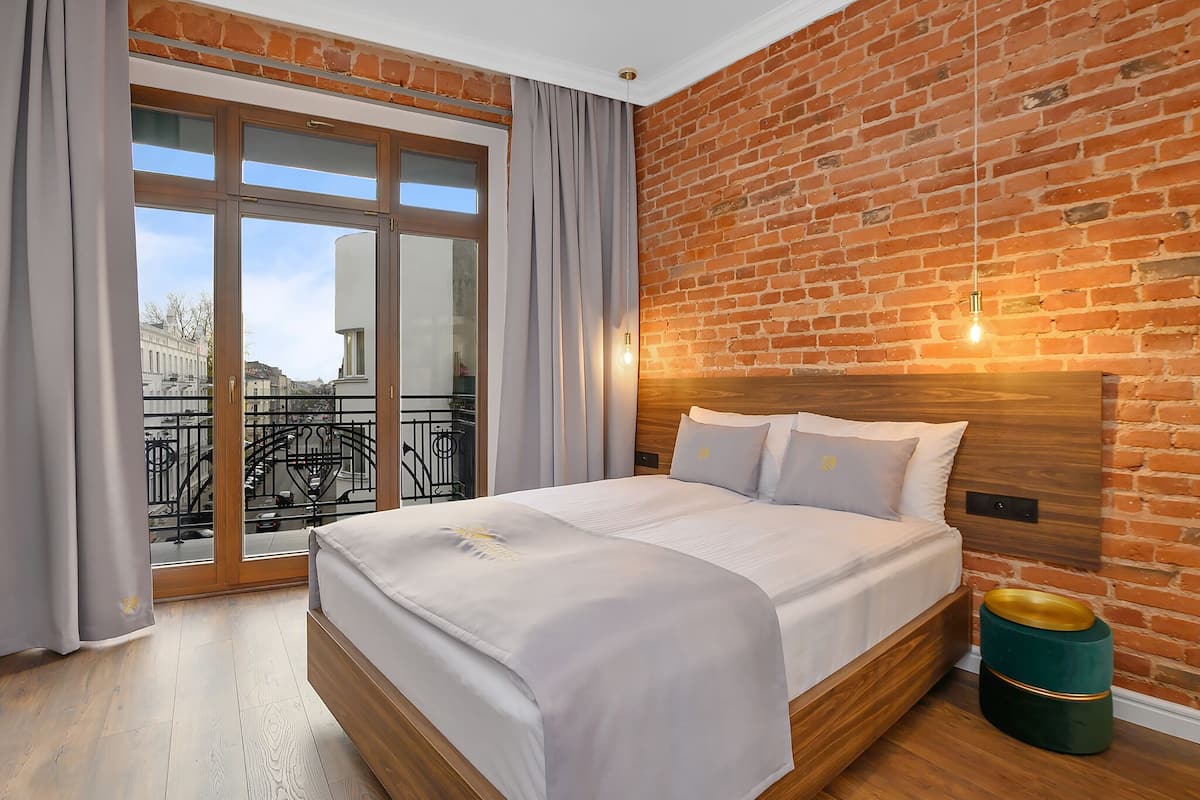 Ein Hotelzimmer mit einem großen Bett, einer Backsteinwand und einem Balkon mit Blick auf Gebäude.
