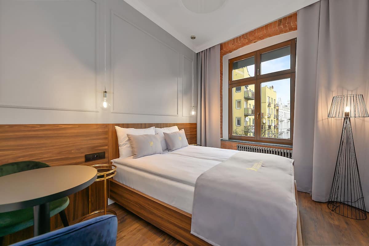 Ein Hotelzimmer mit einem großen Bett, einem runden Tisch und Blick auf die Stadt durch ein Fenster.