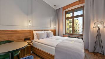 Hotellihuone, jossa on suuri sänky, pyöreä pöytä ja ikkunasta avautuva näkymä kaupunkiin.