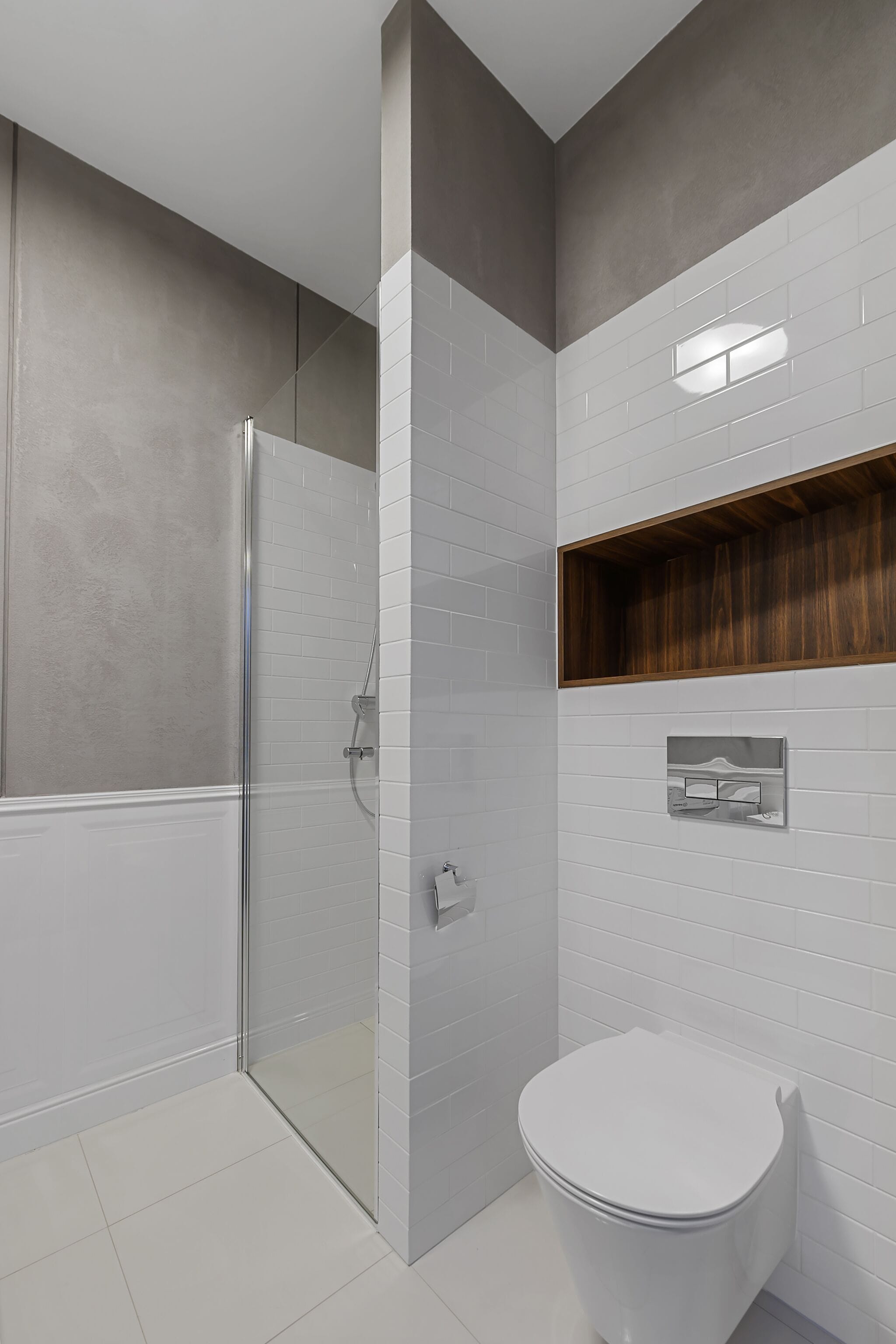 A modern bathroom with a glass shower enclosure, a white toilet, and a wooden shelf above the sink.