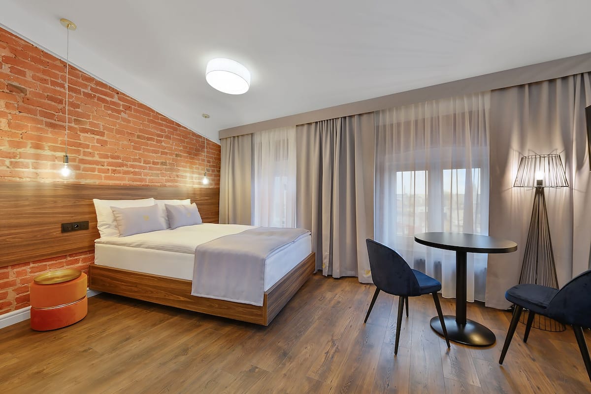 Ein modernes Hotelzimmer mit einer Ziegelwand, einem hölzernen Bett, einem runden Tisch mit zwei Stühlen und einer Stehlampe.