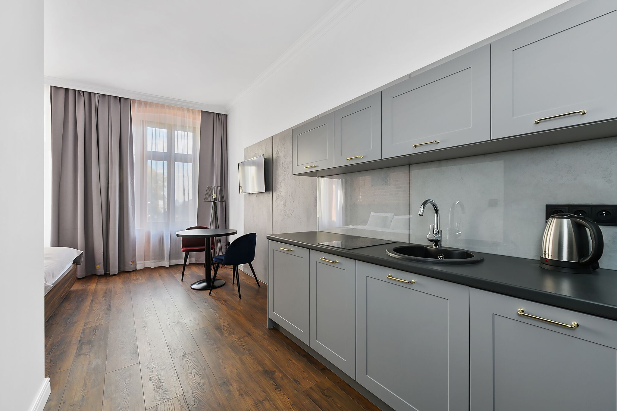 Une cuisine moderne avec des meubles gris, un plan de travail noir et une bouilloire en acier inoxydable.