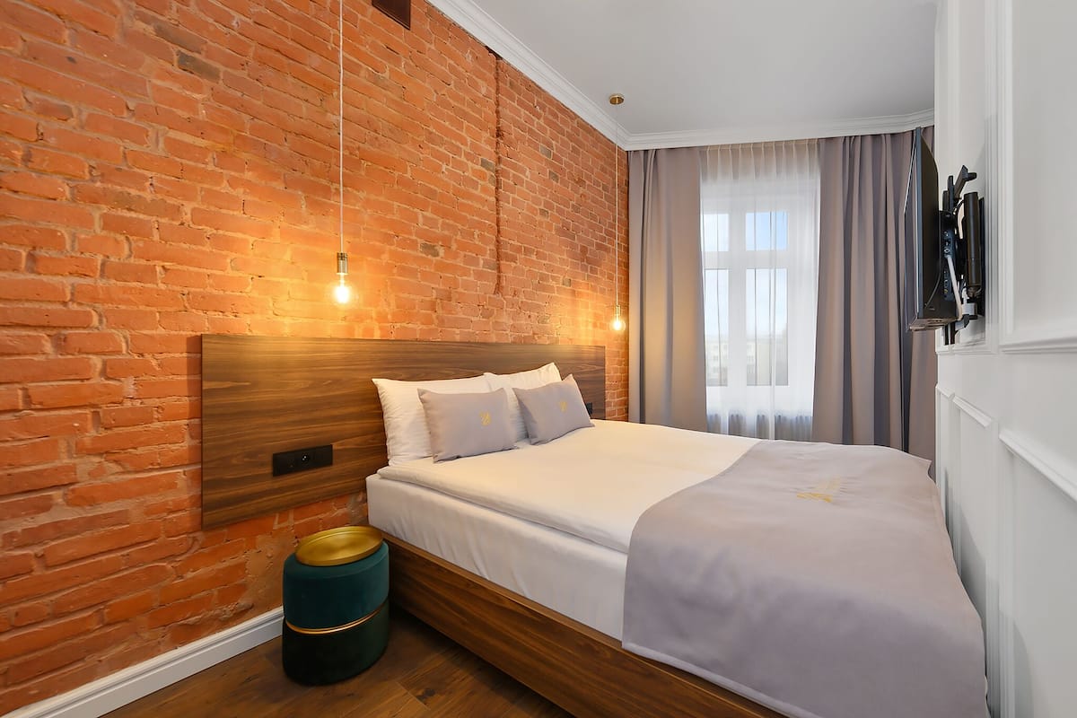 Ein modernes Schlafzimmer mit Backsteinwand, Holz-Kopfteil, Bett mit weißen Leinen und einem grünen Mülleimer.