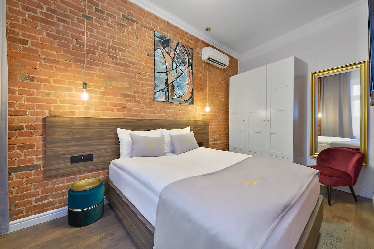Ein Hotelzimmer mit Backsteinwand, einem großen Bett, einem roten Sessel und einem Kleiderschrank.