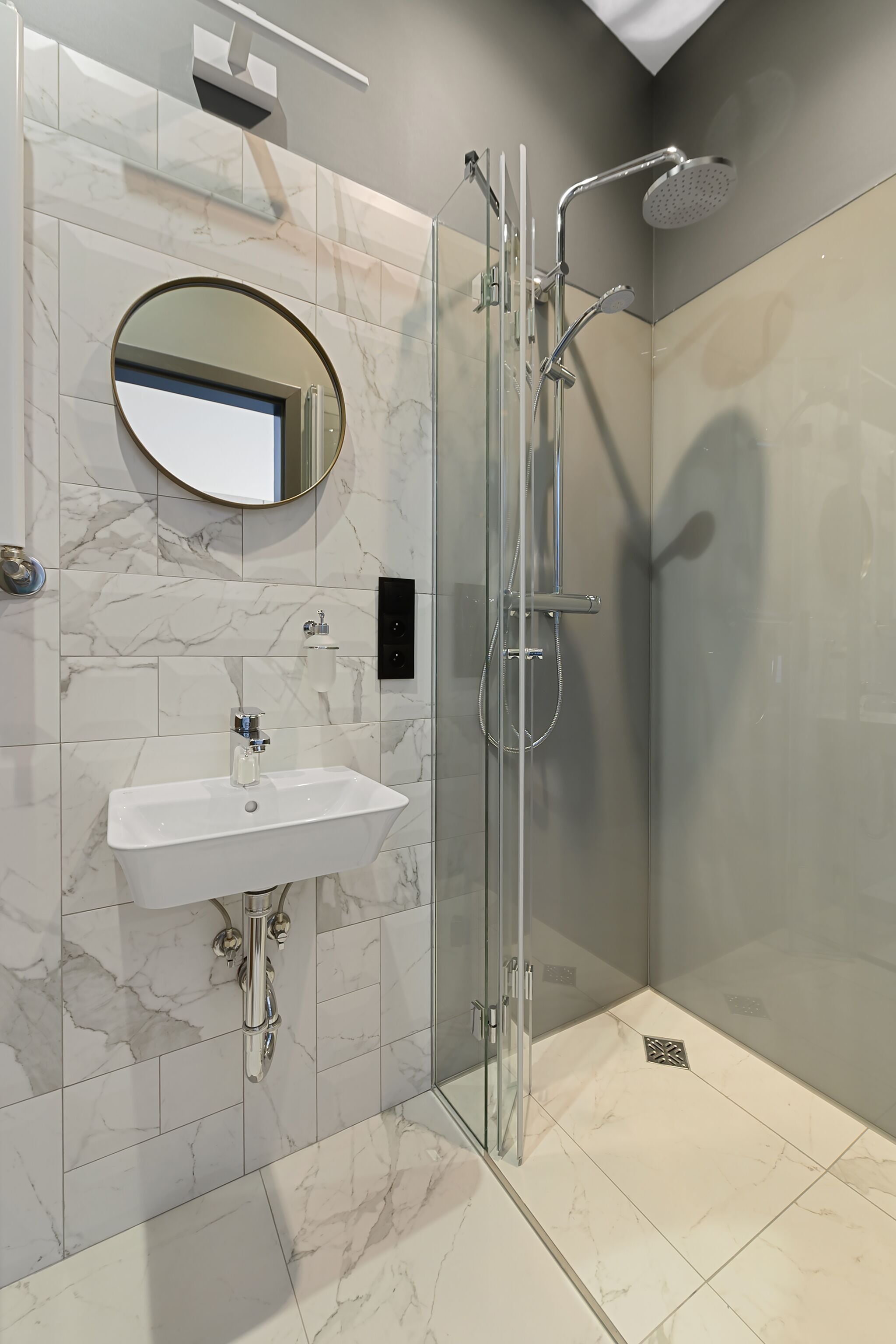 A modern bathroom with a glass-enclosed shower, a white sink, and a marble-tiled wall.