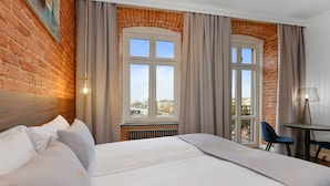 Ein Hotelzimmer mit einem großen Bett, Blick auf die Stadt durch ein Fenster und einem kleinen Tisch mit Stühlen.
