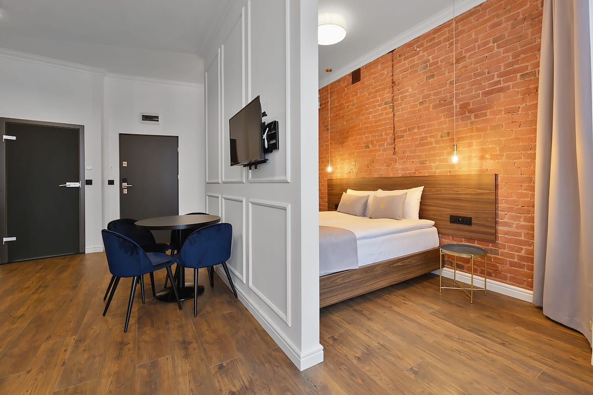 Ein Zimmer mit Bett, einem an der Wand befestigten Fernseher, einem Esstisch mit Stühlen und einer Ziegelwand.