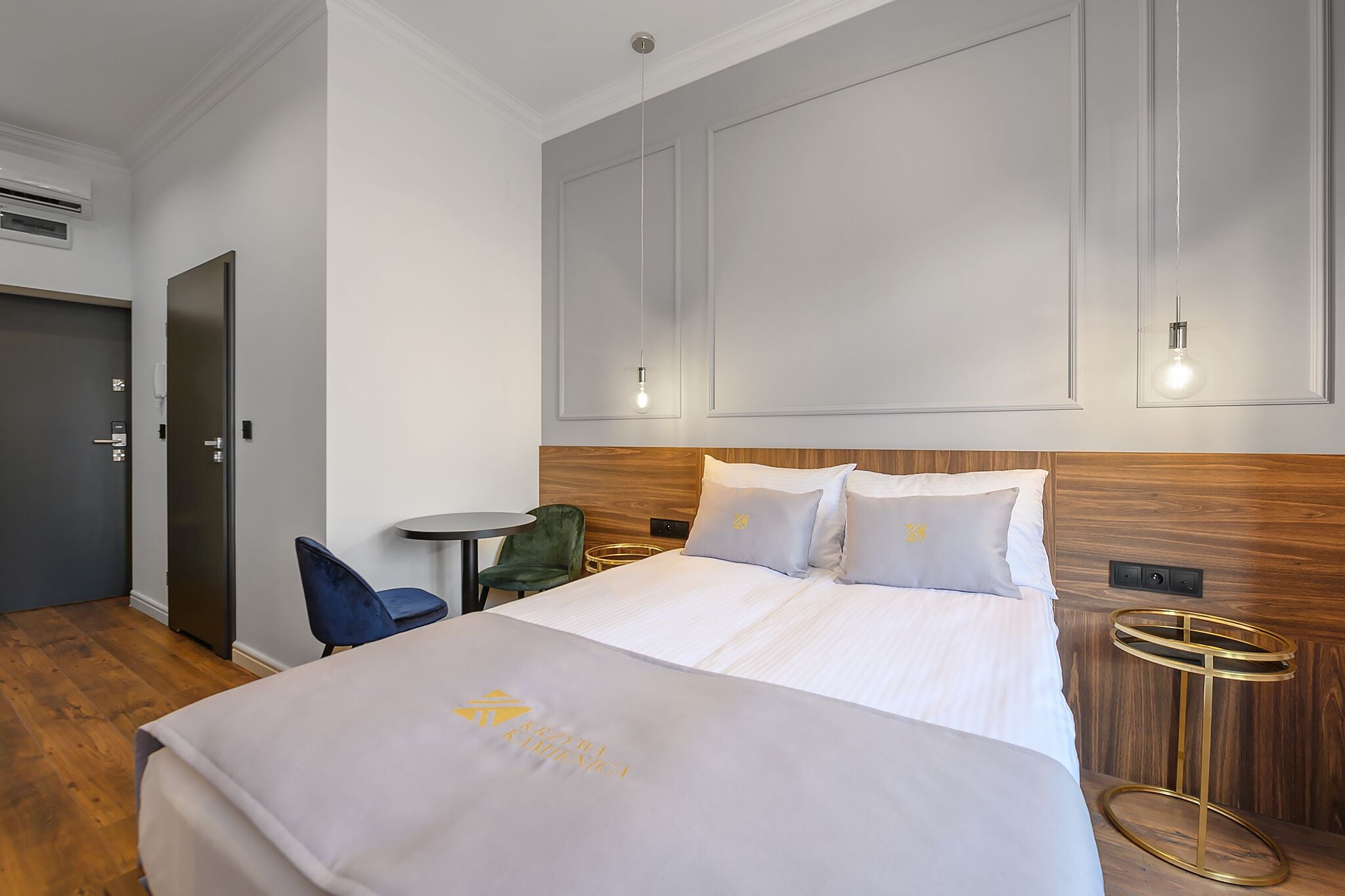 Una camera d'albergo con un letto grande, un tavolino piccolo, una sedia verde e una testiera di legno.