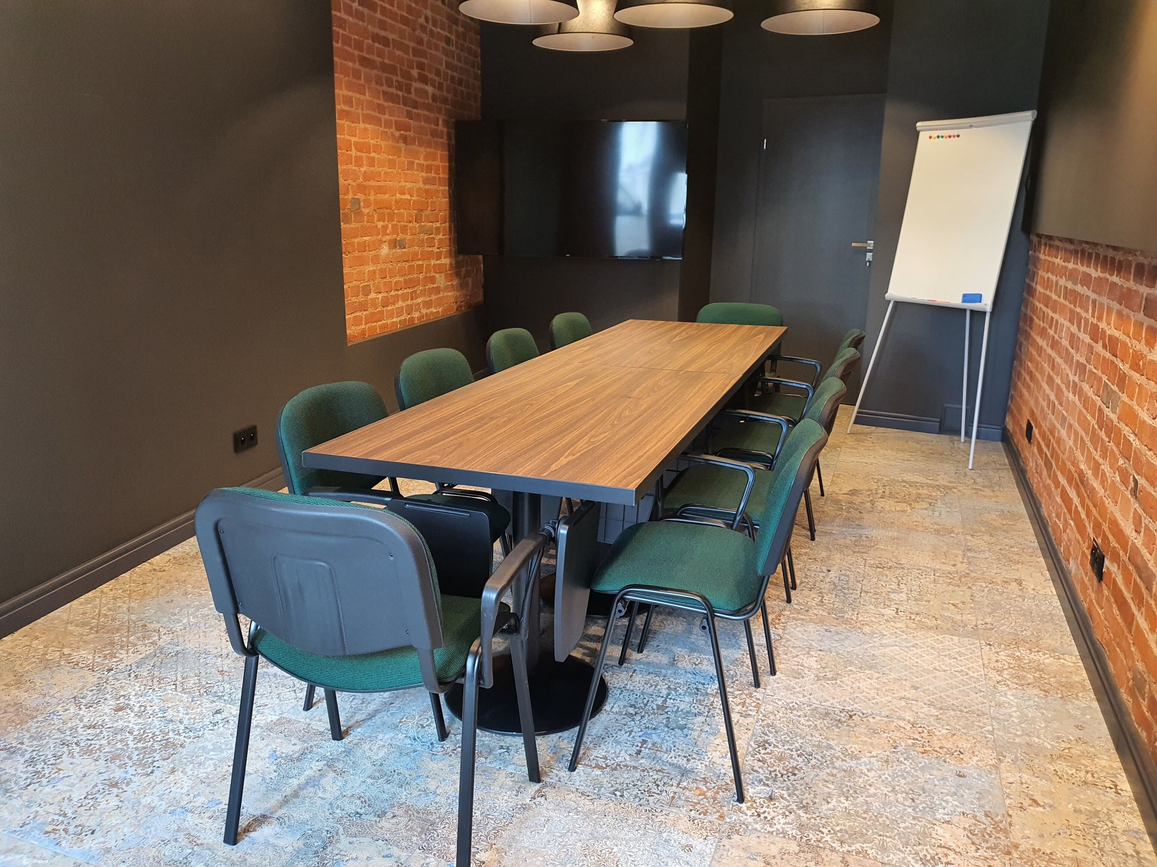 Una sala de conferencias con una larga mesa de madera, sillas tapizadas de verde, una pizarra y un televisor de pantalla plana montado en la pared.