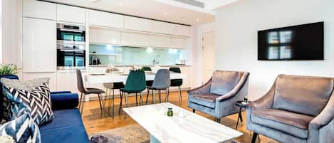 A modern living room with a sofa, armchairs, a coffee table, and a dining area with chairs and a kitchen in the background.