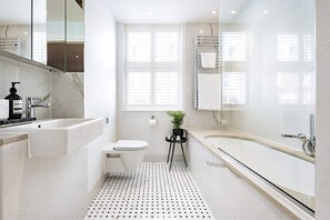 Features a bathtub, sink, and chrome fixtures, with a small mirror and potted plant.