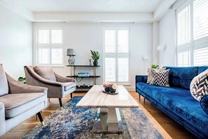 Ein Wohnzimmer mit einem blauen Sofa, zwei Sesseln, einem Couchtisch und einem Bücherregal.