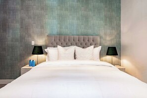 A neatly made bed with a tufted headboard, two bedside lamps, and a nightstand with a bottle and a small object. - The Smooth Velvet - by Out of Office Lifestyle (Greater London)