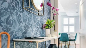 A modern interior with a patterned wall, a mirror, a vase with flowers, a table, chairs, and a pair of boots.