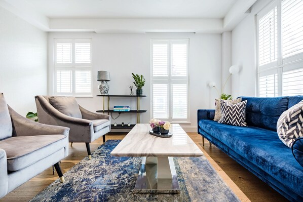 Relax in this stylish living room with a sofa, armchair, and coffee table, set against a beautiful rug and large windows.