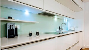 A modern kitchen with white cabinetry, a built-in espresso machine, and a glass-top counter.