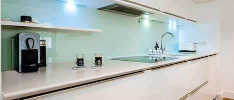 Una cocina moderna con armarios blancos, una cafetera espresso integrada y una encimera de vidrio.