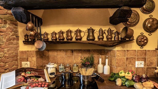 Una cocina con pared de ladrillo, repisas de madera con utensilios de cocina y verduras frescas en la encimera.