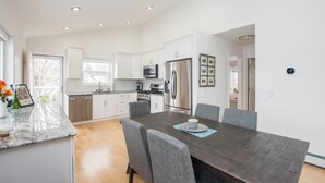 Une cuisine moderne avec des meubles blancs, des appareils en acier inoxydable et un coin repas comprenant une table en bois foncé et des chaises grises.