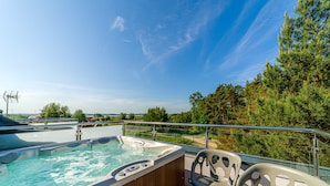 A hot tub on a deck with chairs, overlooking a forest and water. - Wicie Residence (Darlowo)