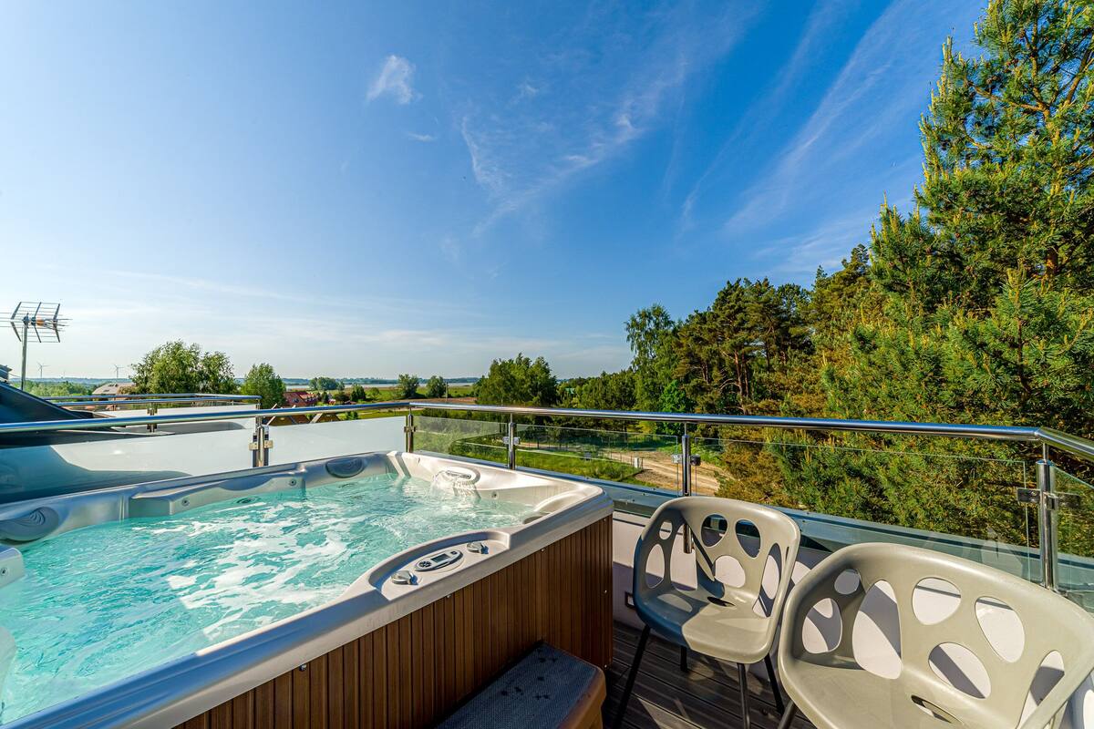 Un jacuzzi en una terraza con sillas, con vistas a un bosque y al agua.