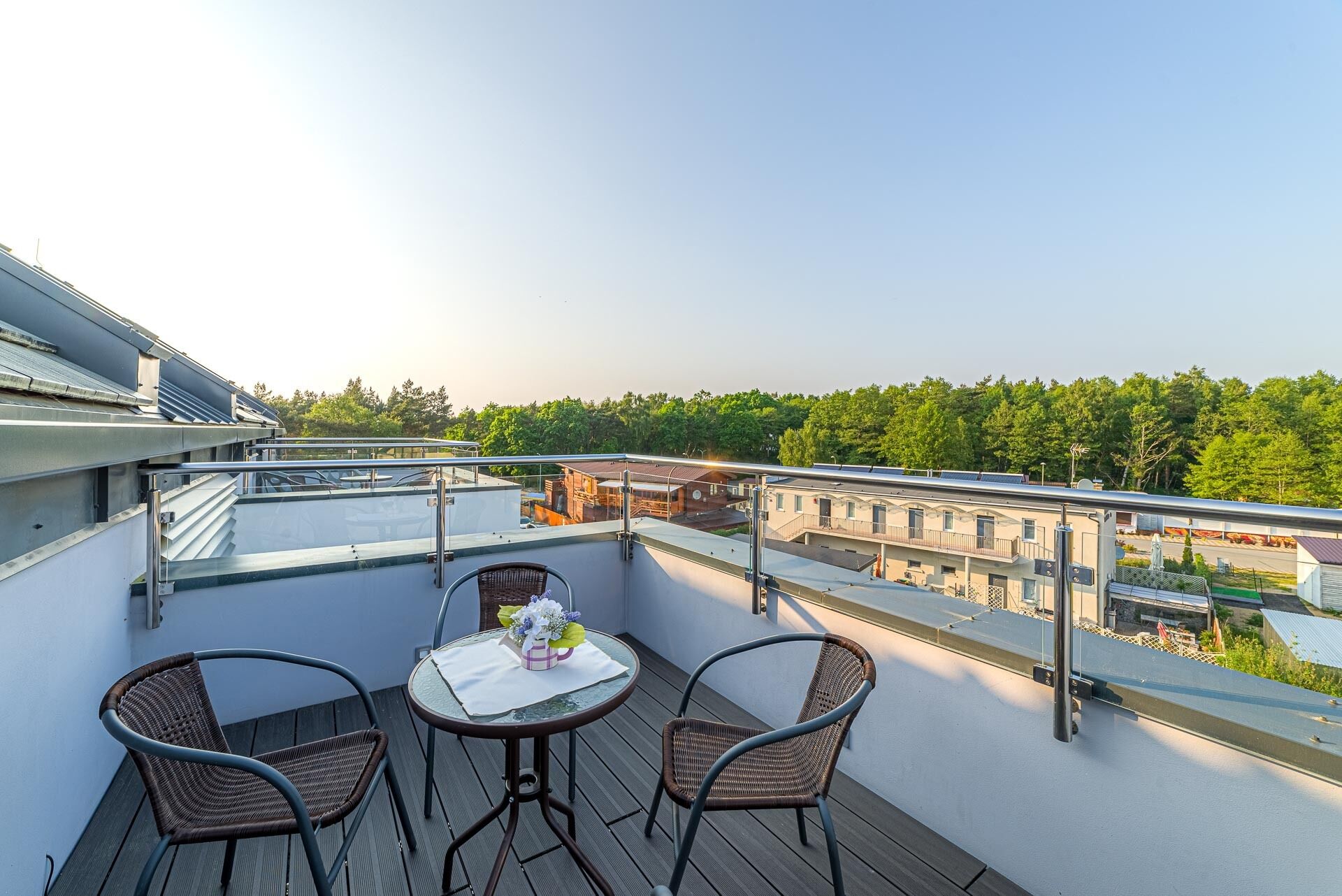 A balcony with two wicker chairs and a small table, overlooking a residential area with trees and buildings.