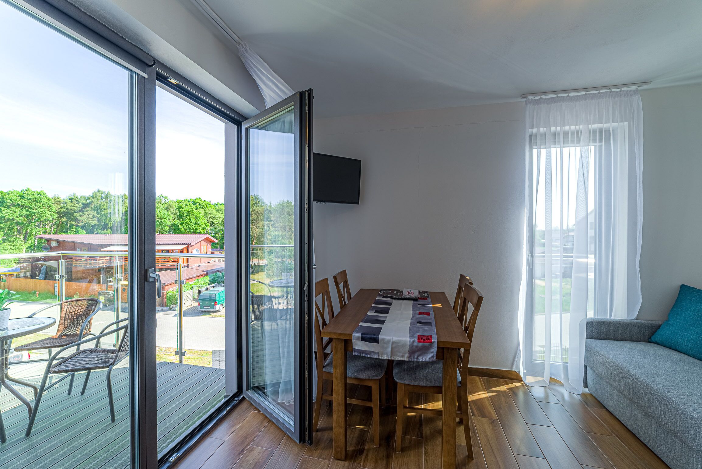 A dining area with a table and chairs, a sofa, and a TV on the wall.