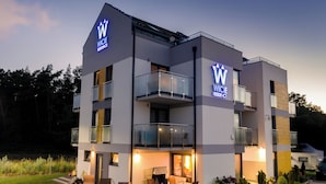 A modern hotel with a prominent 'W' logo, a balcony with glass railings, and a well-lit outdoor seating area. - Wicie Residence (Darlowo)