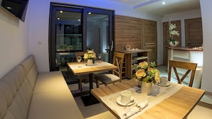 A modern dining area with a wooden table set for two, a sofa, and a kitchen in the background. - Wicie Residence (Darlowo)