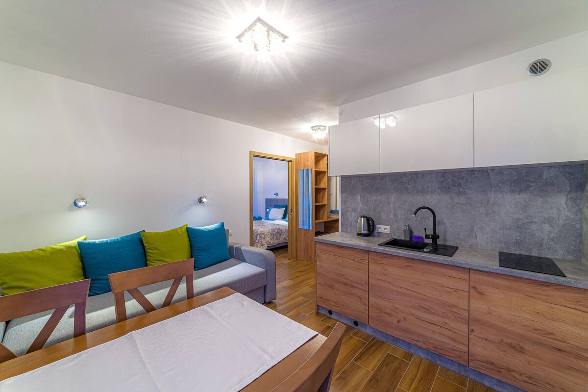 Un espacio habitable pequeño con kitchenette, un sofá con cojines de colores y una pequeña zona de comedor.