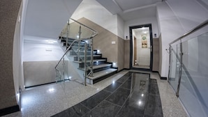 A modern interior with a glass staircase, a hallway leading to a door, and a tiled floor. - Wicie Residence (Darlowo)