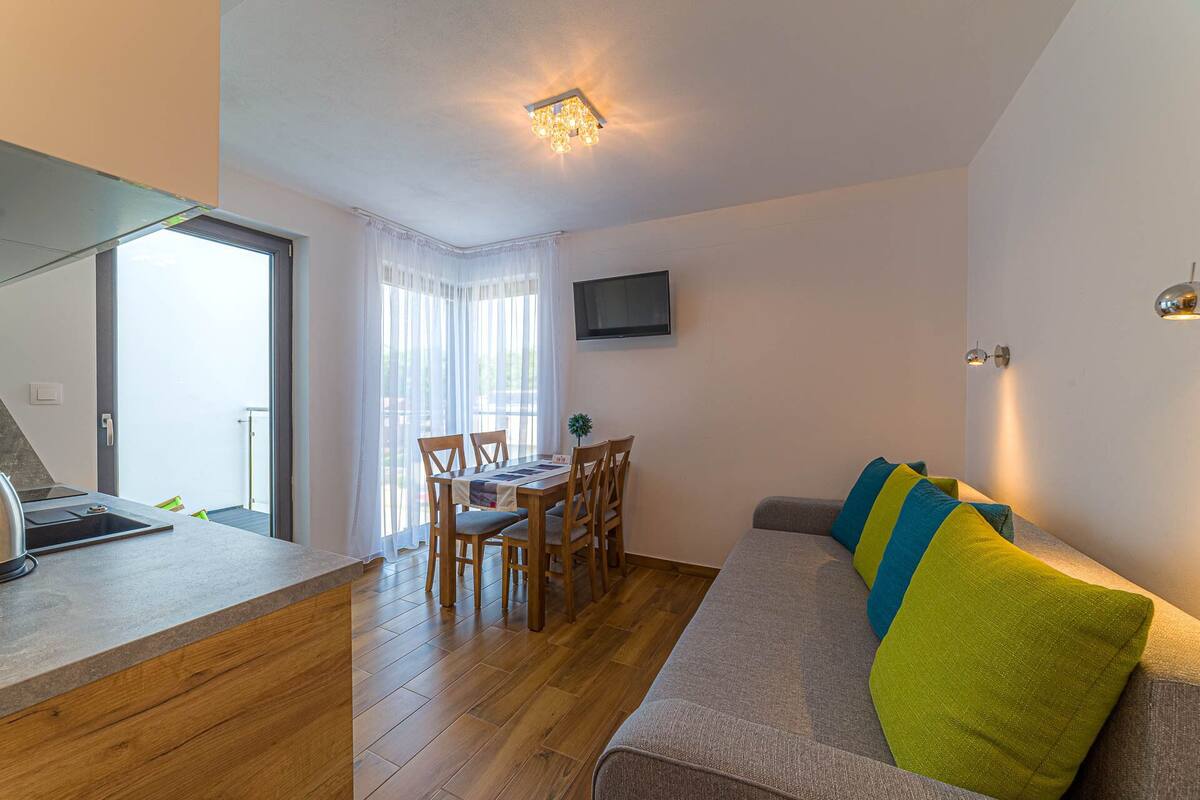 Una sala de estar moderna con un sofá, una mesa de comedor y sillas. Hay un televisor montado en la pared y una lámpara en el techo.