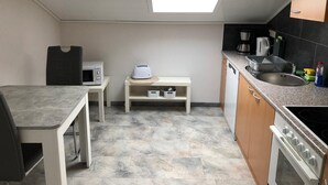 Une cuisine compacte équipée d’un four à micro-ondes, d’un grille-pain et d’une machine à café. On y trouve une petite table et un banc avec un espace de rangement en dessous. La cuisine est dotée d’une lucarne et offre une vue sur l’extérieur.