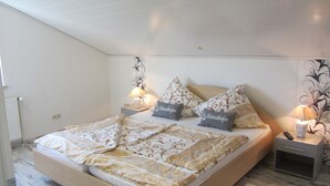 Une chambre à coucher avec un lit, deux tables de chevet avec des lampes, un radiateur et un mur orné d’un motif floral.