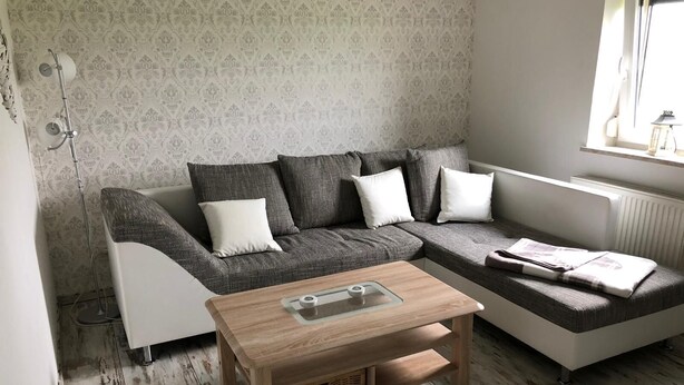 Un salon moderne avec un canapé gris, des coussins blancs, une table basse en bois et un papier peint à motifs.