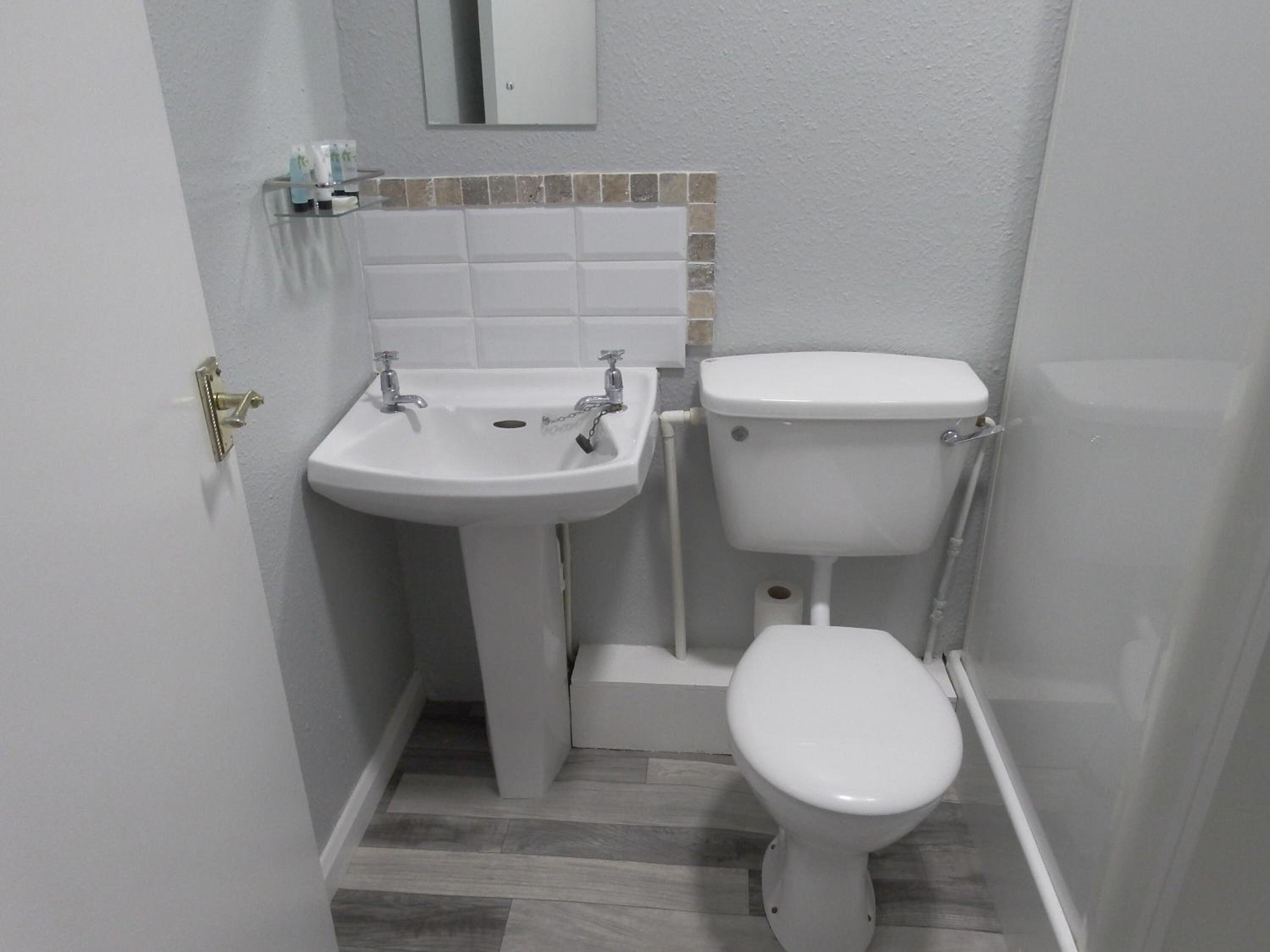 Un baño pequeño con un lavamanos blanco, inodoro y un espejo pequeño sobre el lavamanos.