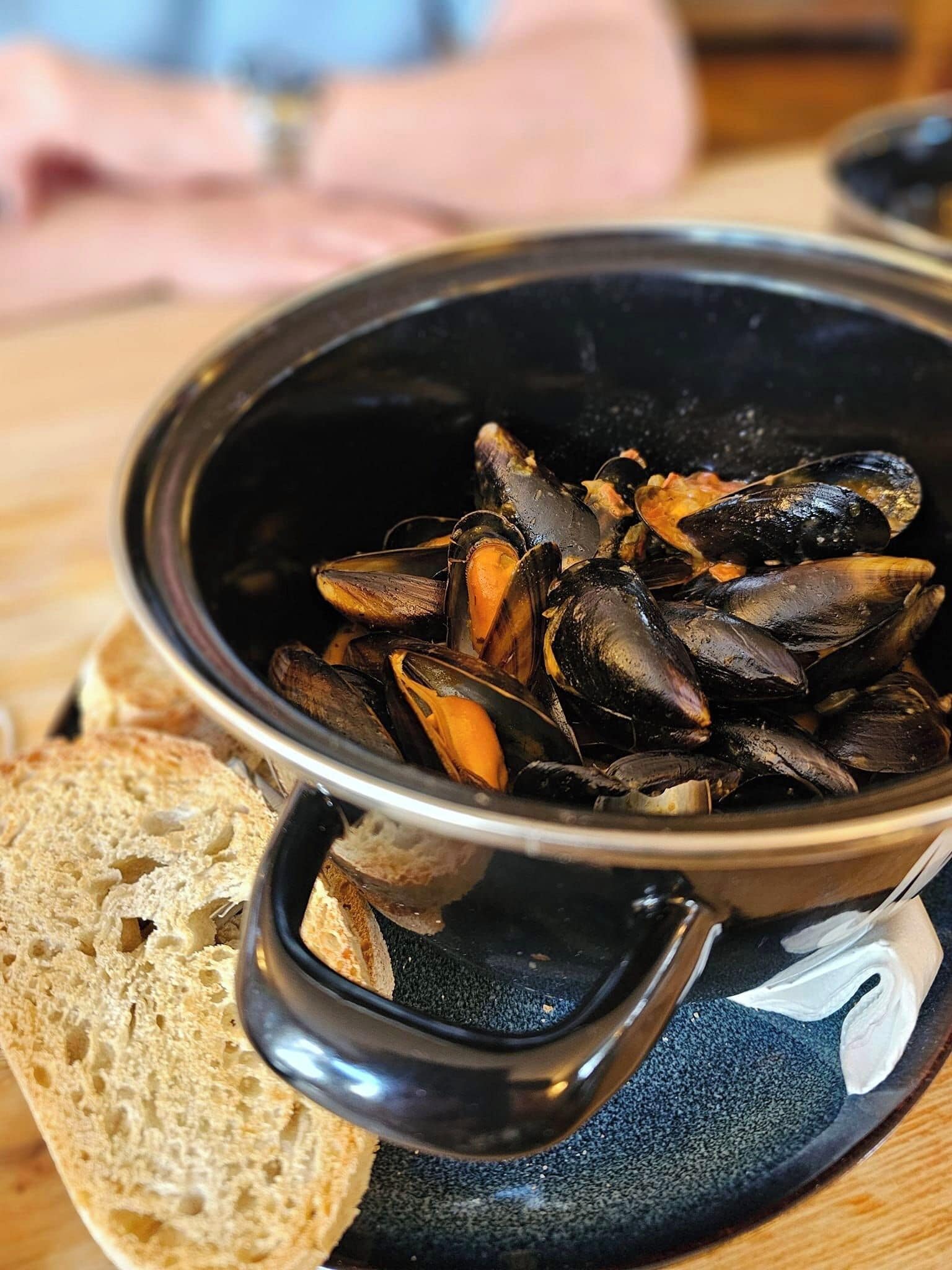 A bowl of mussels with a piece of bread on the side.