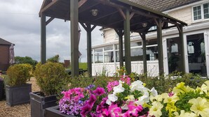 A covered outdoor area with a wooden structure, surrounded by potted plants and flowers. - The Haven Inn (Barrow upon Humber)