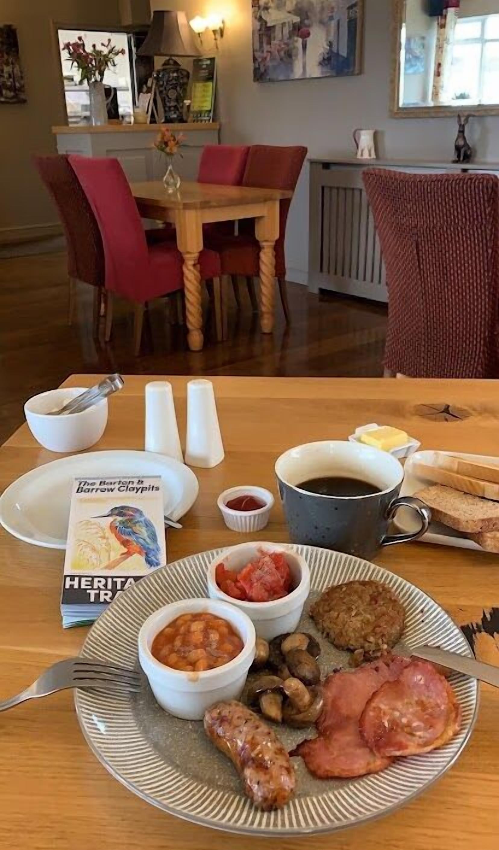 A dining table with a plate of food, including sausages, ham, beans, and a cup of coffee.